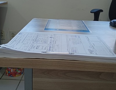 Processo de pagamento (PROPAG) de serviço contínuo, com grande volume de documentos impressos empilhados sobre uma mesa.
